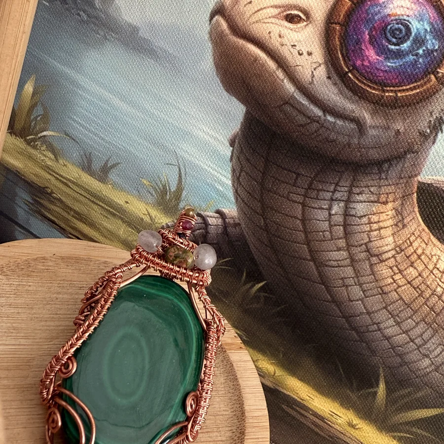 Copper wire-wrapped green stone pendant displayed beside colourful art.