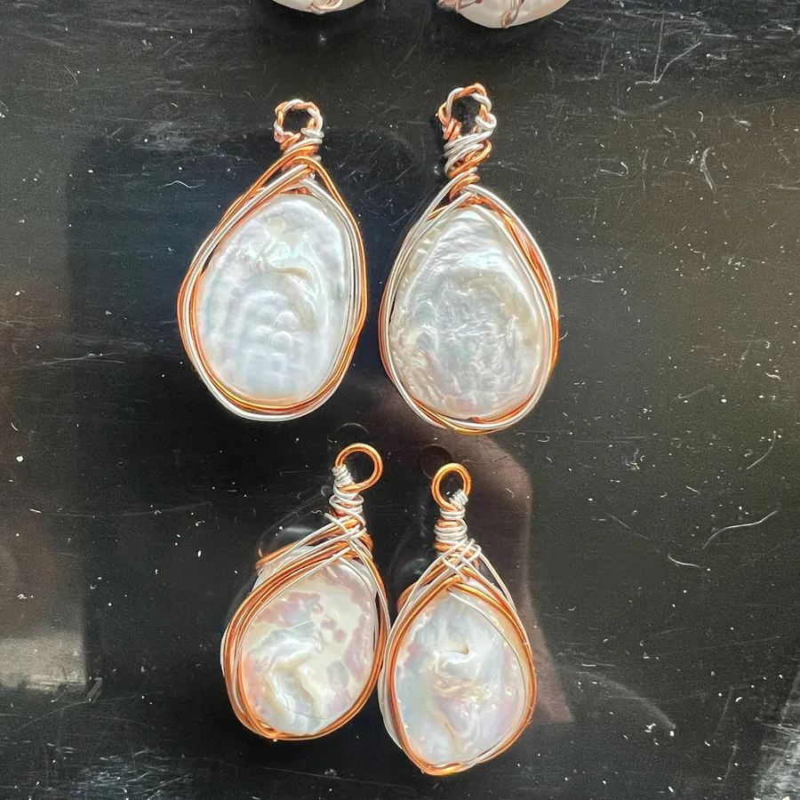 Pearl-toned copper wire-wrapped jewellery pieces on a dark work surface.