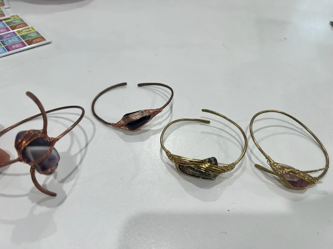 Wire wrapped rings and jewellery pieces arranged on a white work surface.